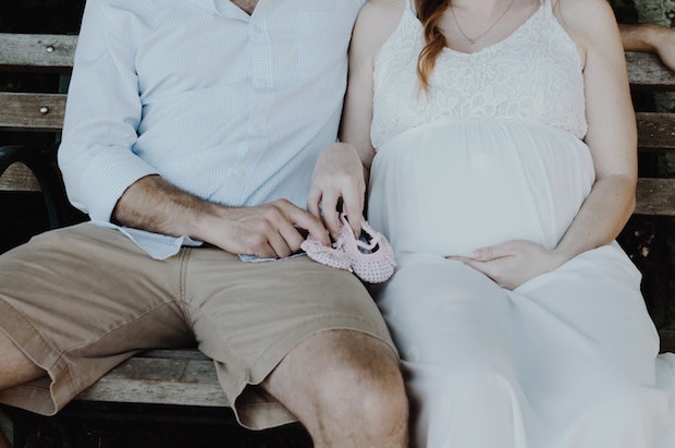 two expectant parents sitting on a bench, holding pink baby shoes