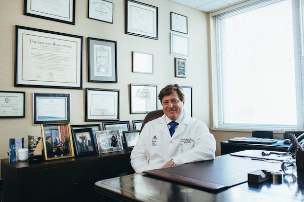 A doctor sitting in front of a wall of certificates