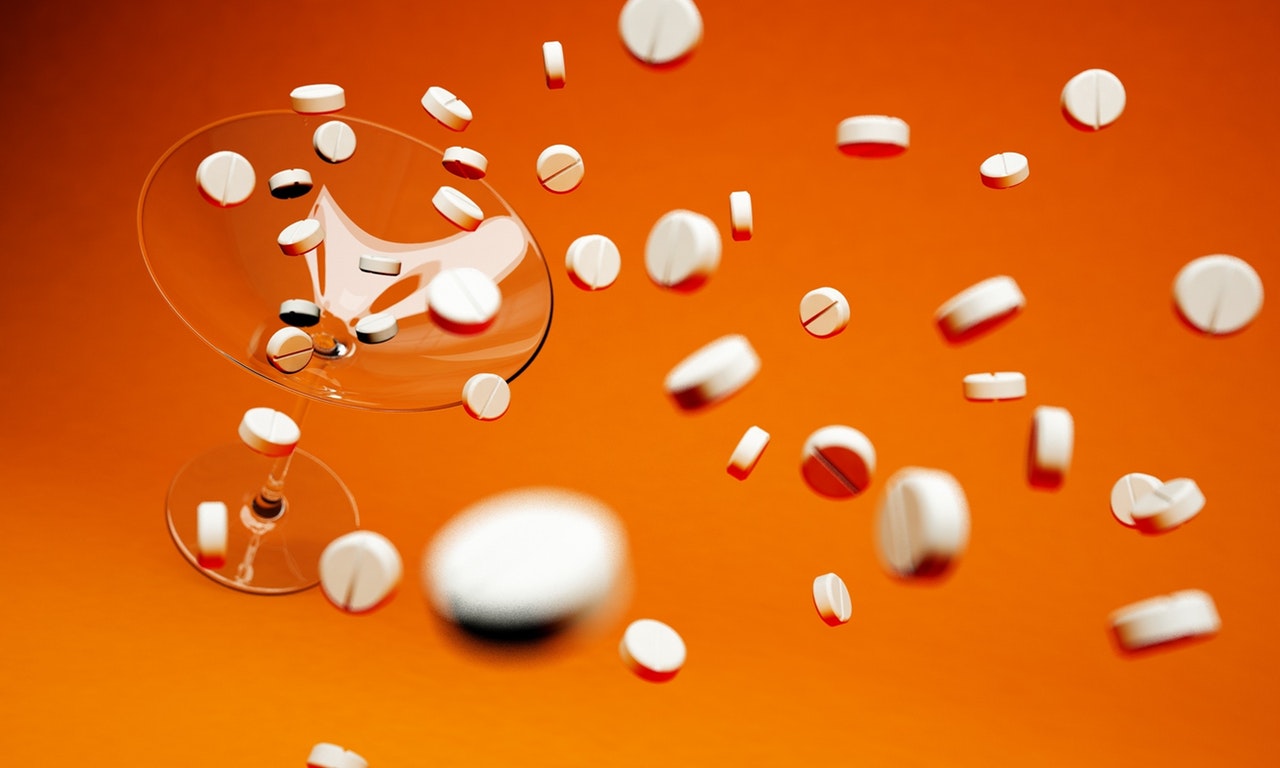 Dynamic image of white round pills flying out of a glass against an orange background.