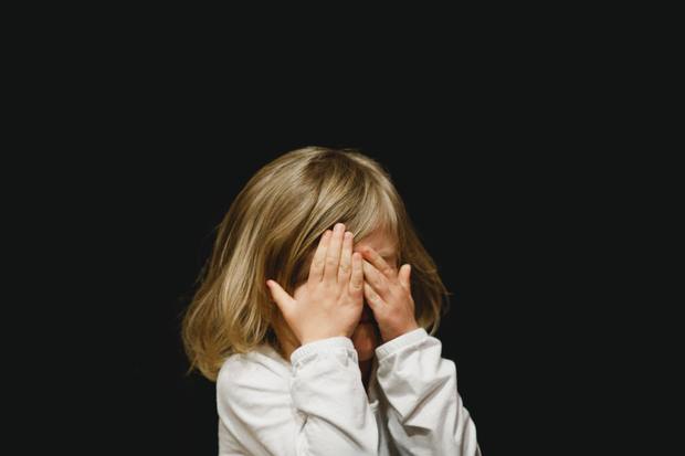 a small child covering her face with her hands