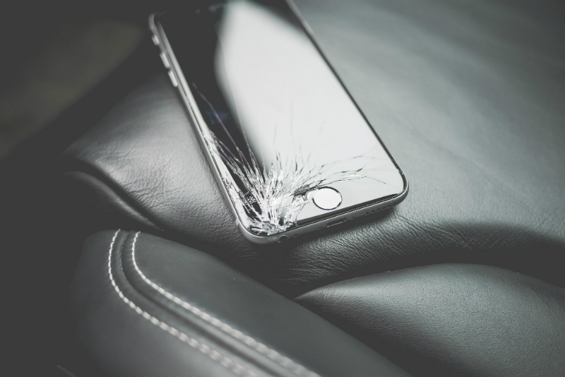 A broken iPhone is on top of a piece of leather furniture.