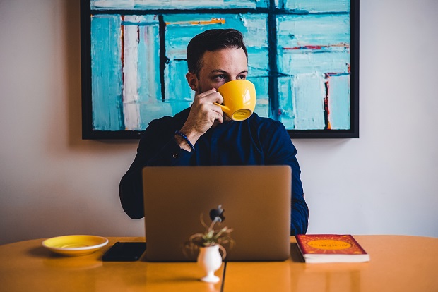 a man drinking out of mug in front of a laptop